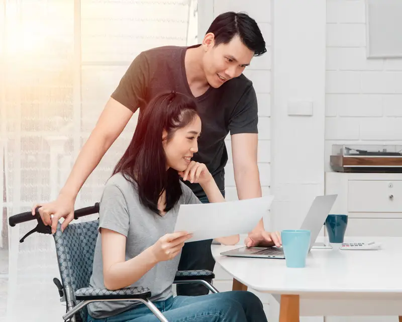 Woman in a wheel chair at a laptop, review paperwork with her husband