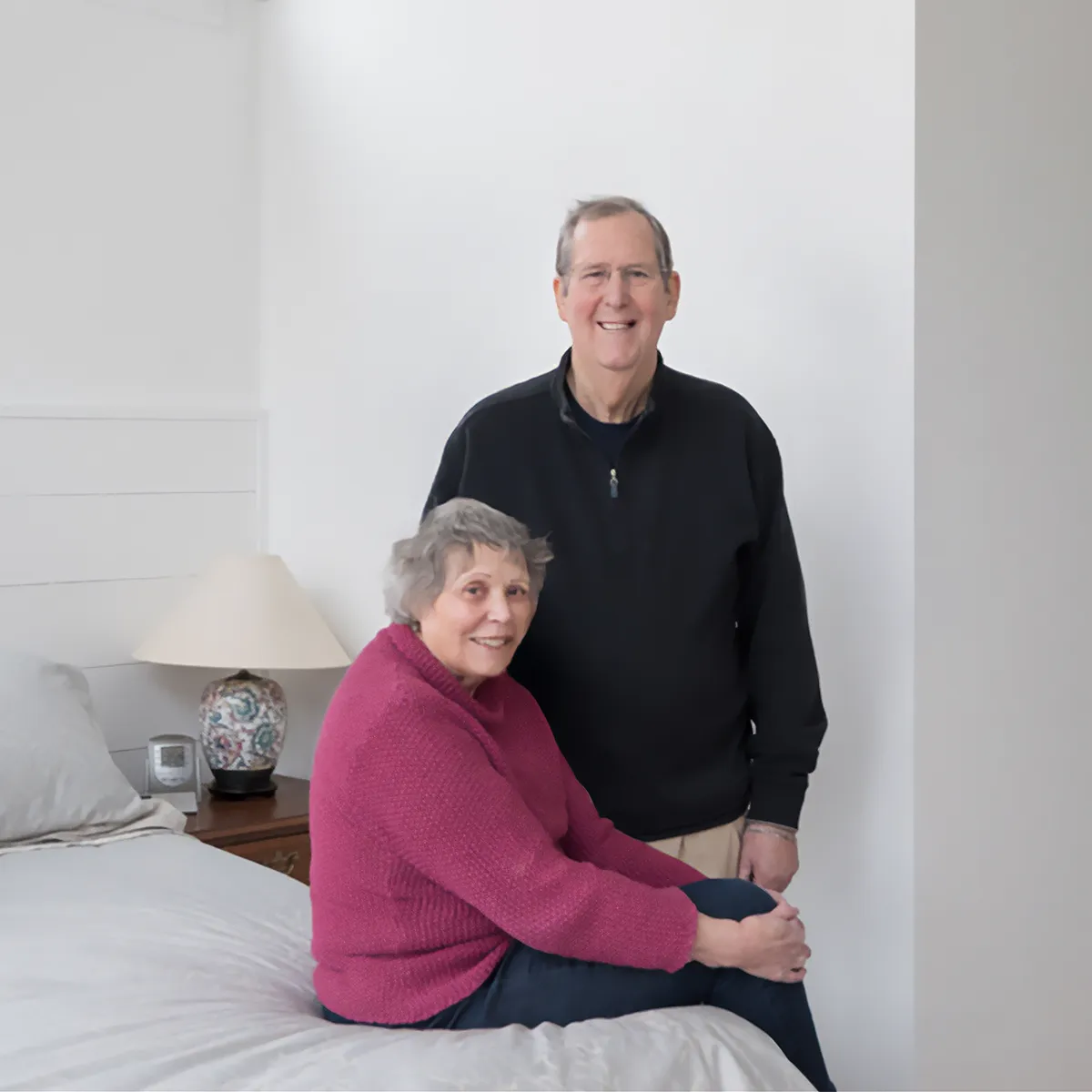 senior couple in newly remodeled space, wife sitting on bed, husband standing, both smiling