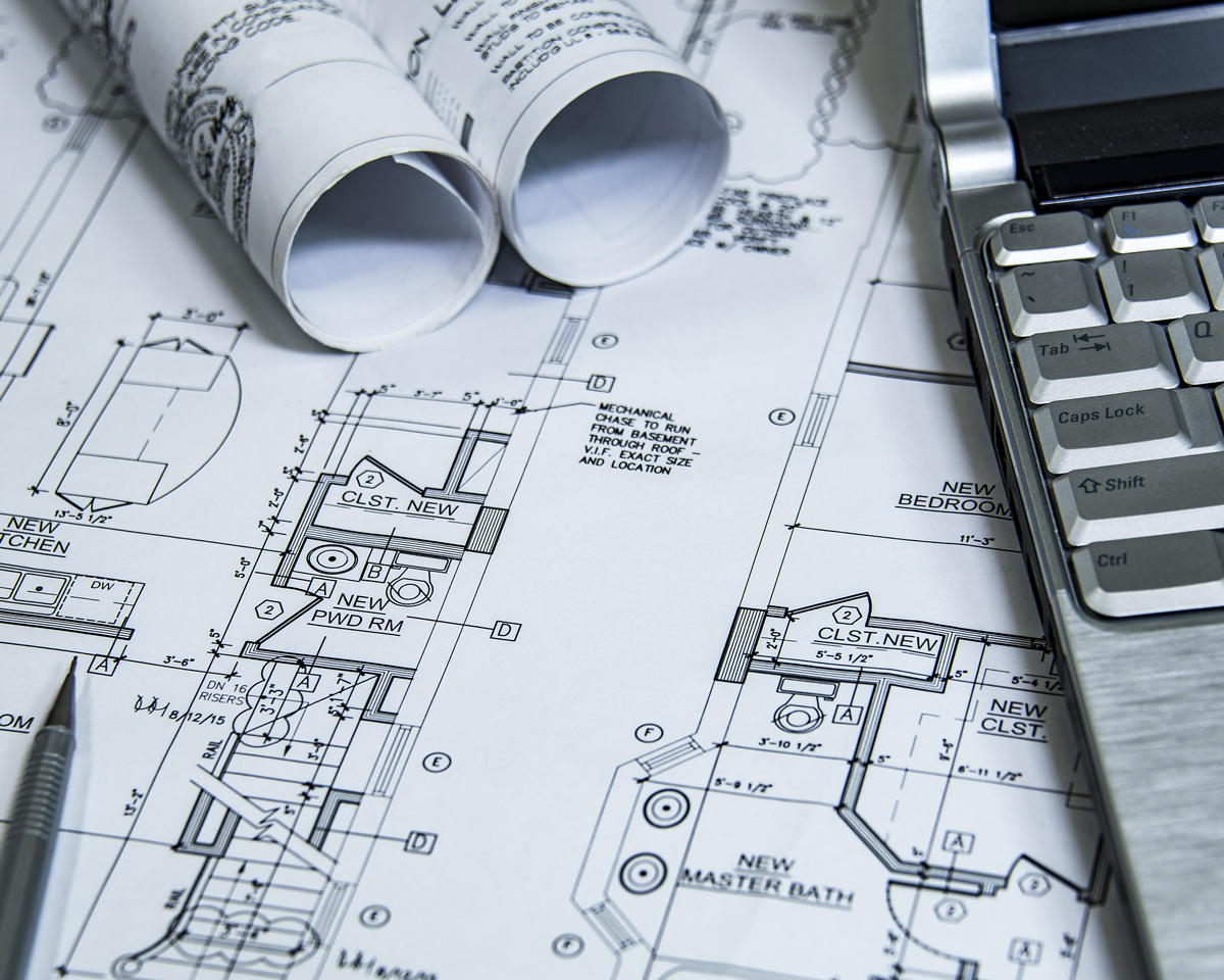 blue prints for home build with bathroom on table with additional rolled blueprints and laptop
